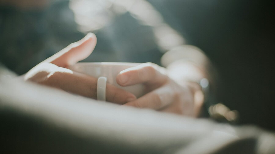 Hands cradling a warm mug by a window in morning light, a calm pause to reduce stress