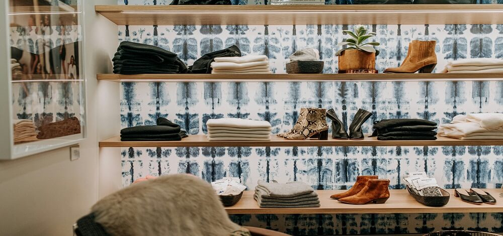Folded organic cotton clothing in neutral tones on a shelf in soft daylight.