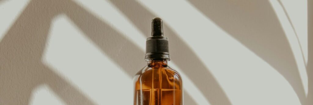 Amber glass dropper bottle of beard care oil on a windowsill, part of a Grooming and Shaving routine