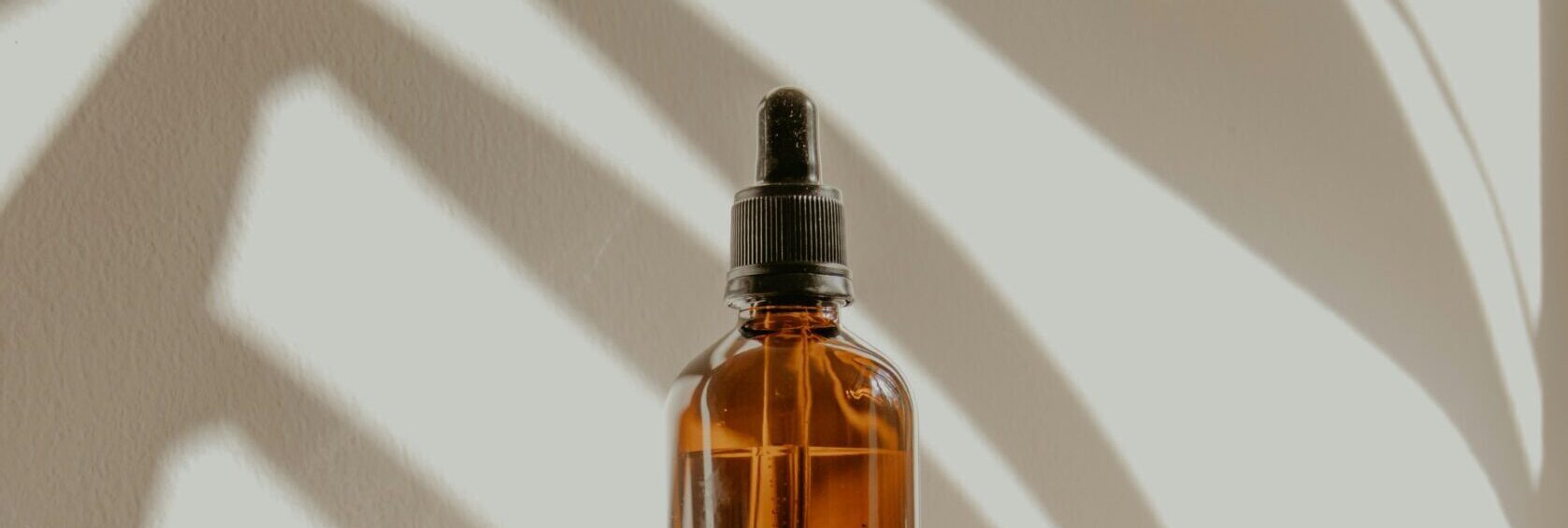 Amber glass dropper bottle of beard care oil on a windowsill, part of a Grooming and Shaving routine